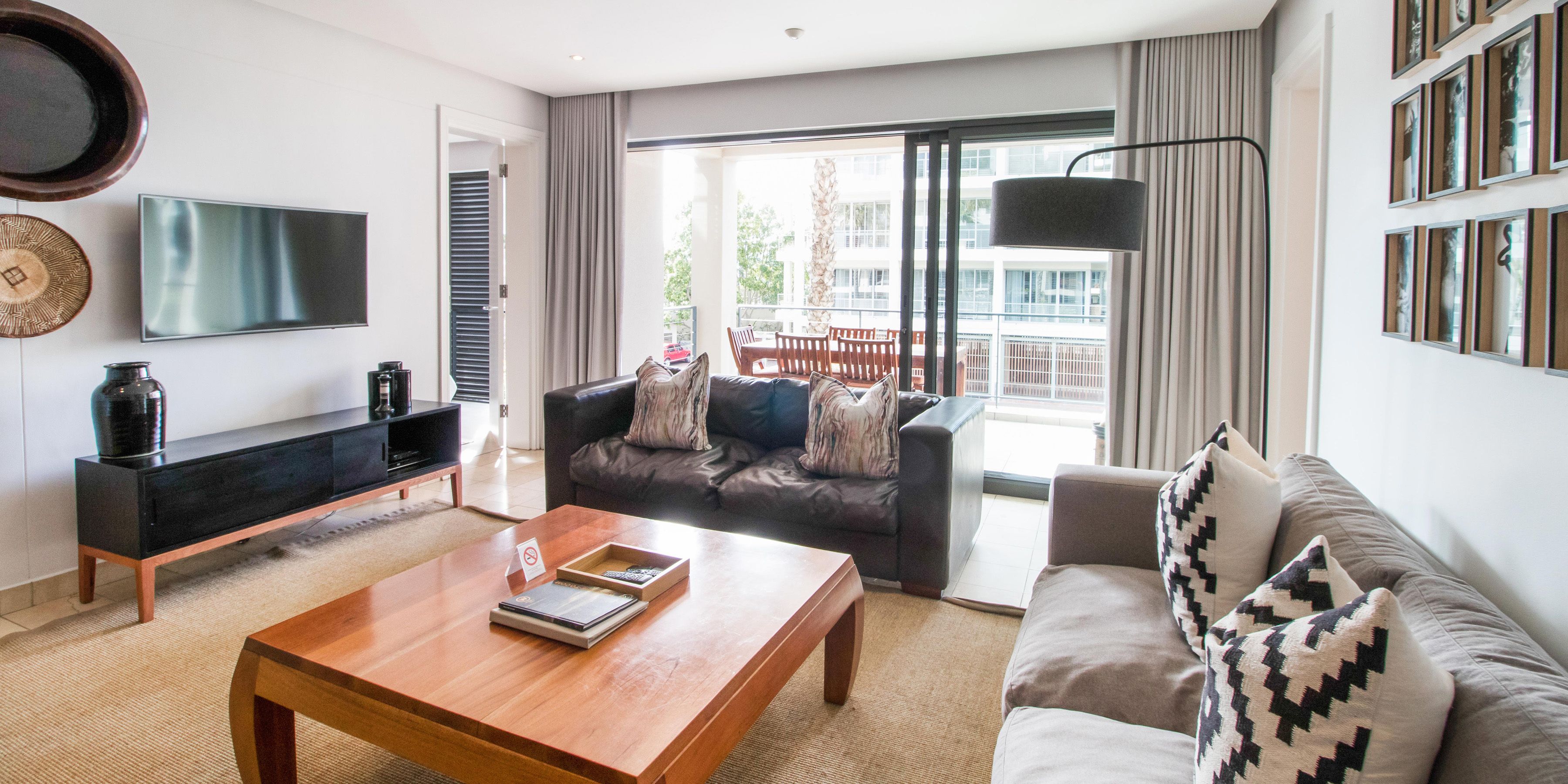 A modern living room with a flat-screen TV, a wooden coffee table, a sofa, and a balcony with a view of buildings.