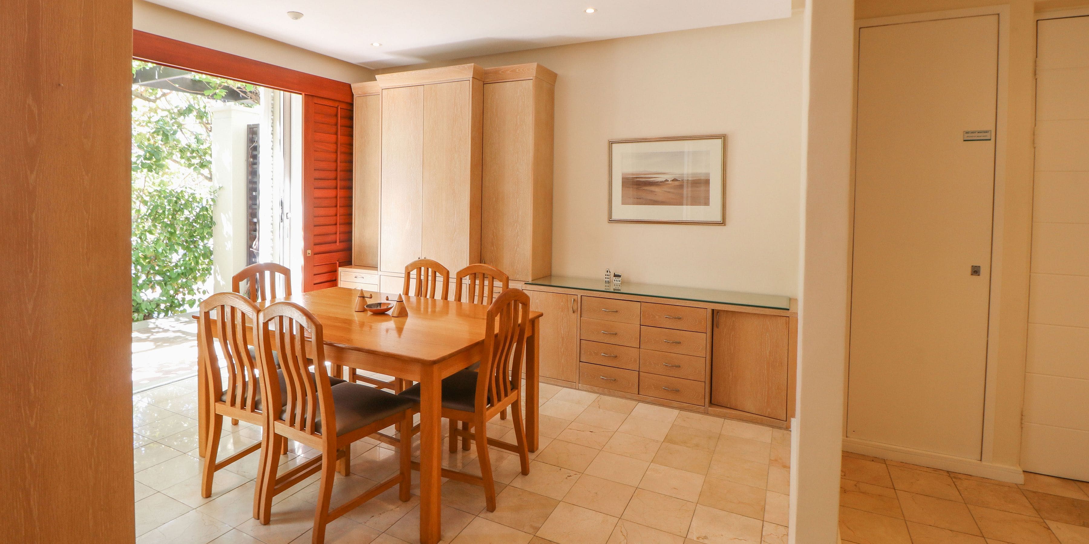 Un comedor con mesa y sillas de madera, una cocina con armarios, y un cuadro enmarcado en la pared.