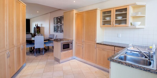 A modern kitchen with wooden cabinets, a granite countertop, and a built-in oven. - Waterfront Village (Cape Town)