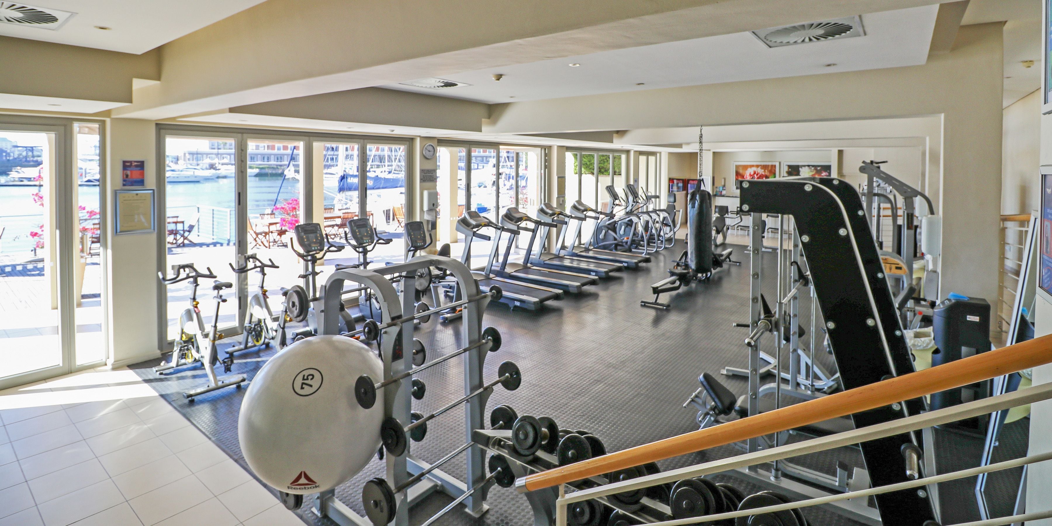 A gym with various exercise equipment, large windows, and a view of the outside.