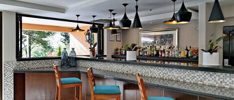 A modern kitchen with a bar area, wooden bar stools, black pendant lights, and a view of the outdoors.