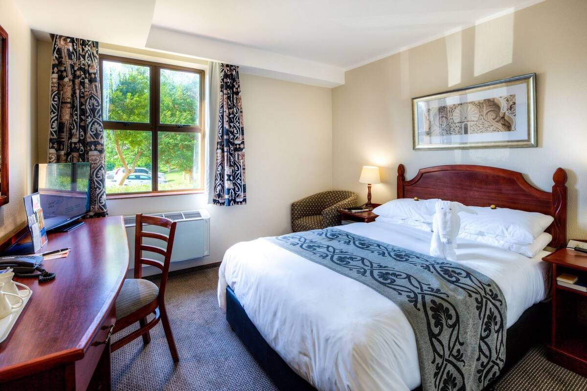 Une chambre d’hôtel avec un lit, un bureau, une chaise et une fenêtre avec des rideaux.