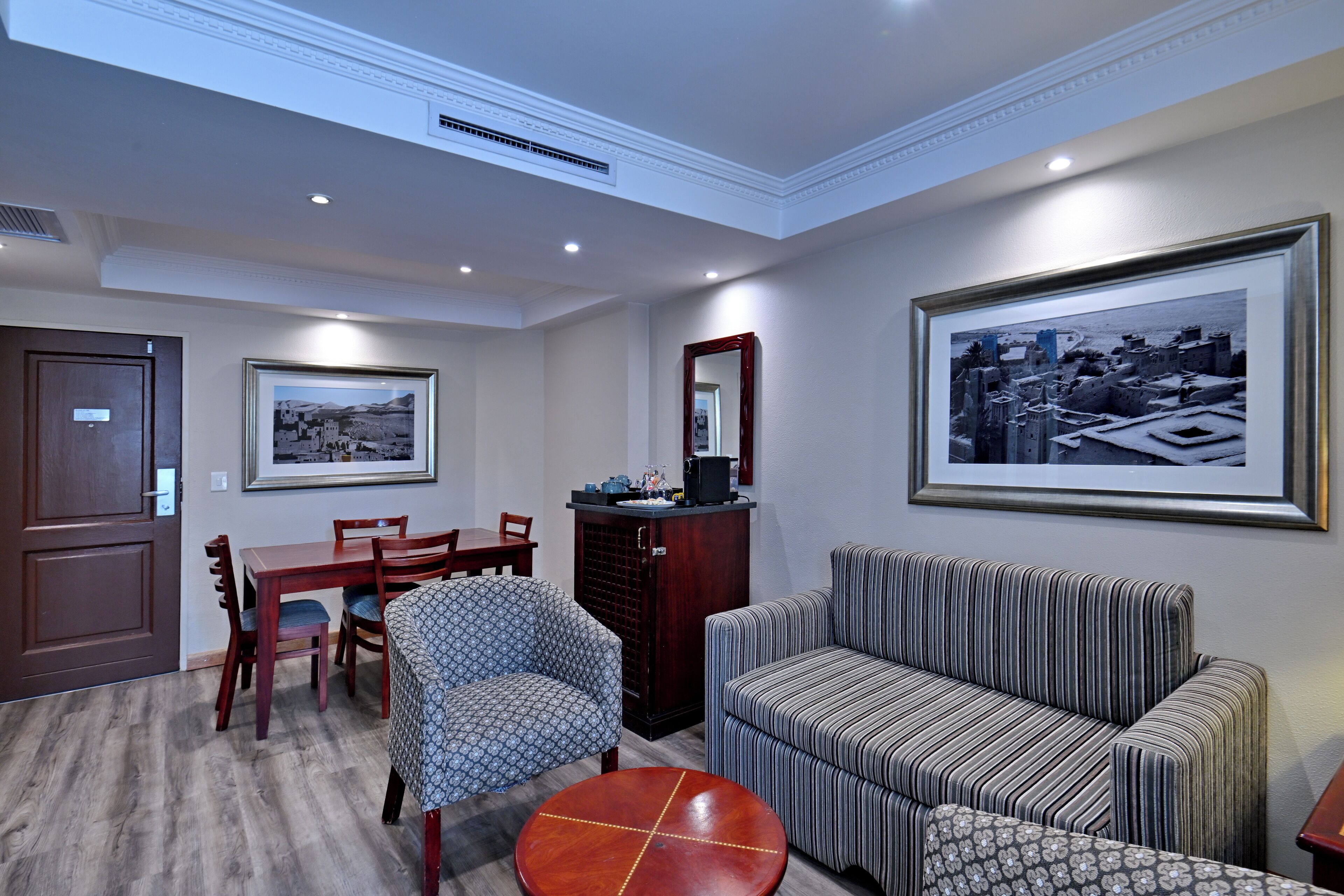 A hotel room with a dining area, a sofa, a small table, and a large framed picture on the wall.