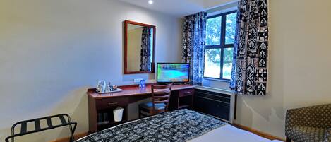 A hotel room with a bed, desk, chair, and a window with patterned curtains.