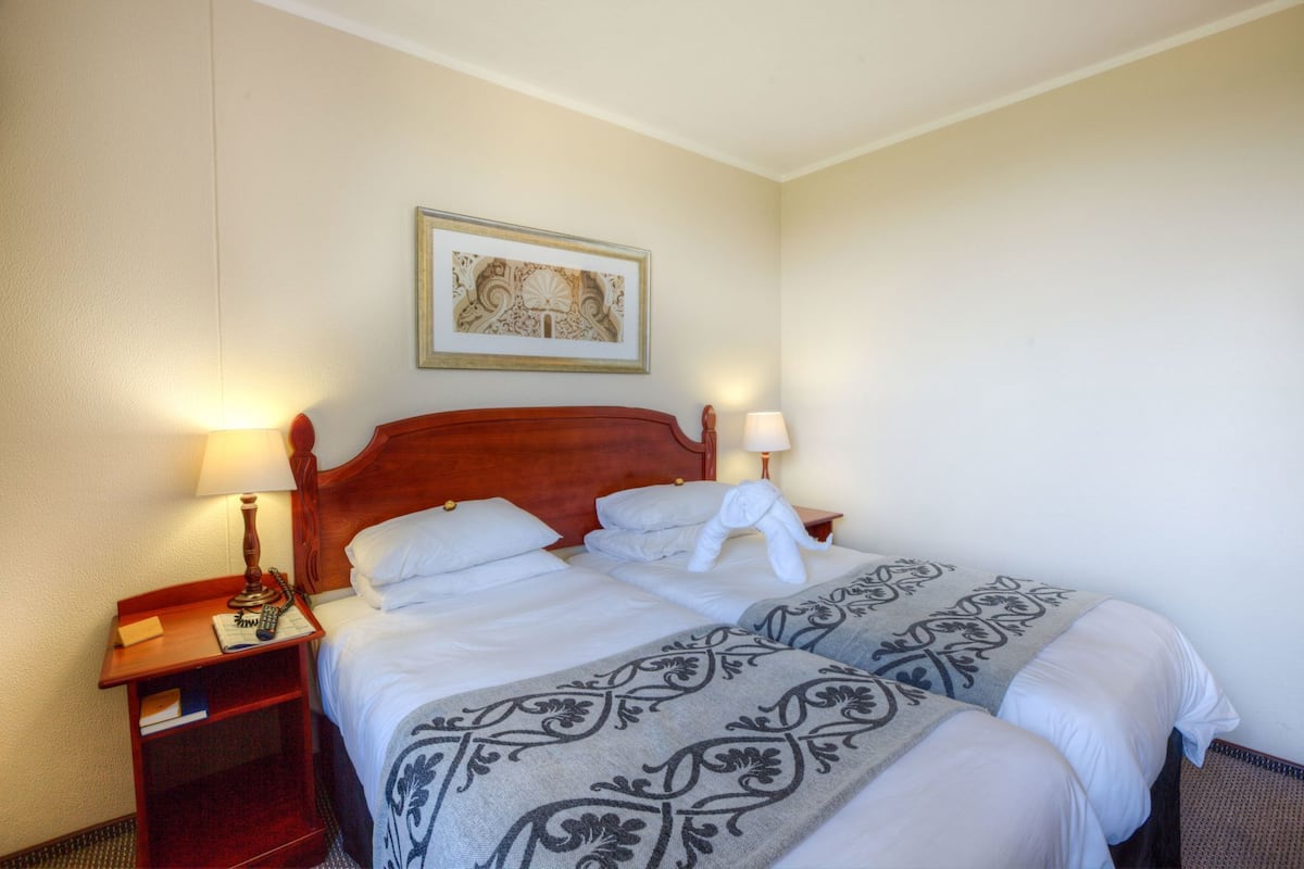 A hotel room with a wooden bed, two bedside tables, a framed picture on the wall, and a patterned bedspread.