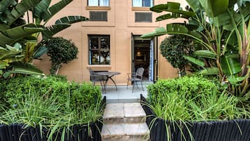 A building with a beige exterior, a patio with a table and chairs, and lush greenery including banana plants and bushes.
