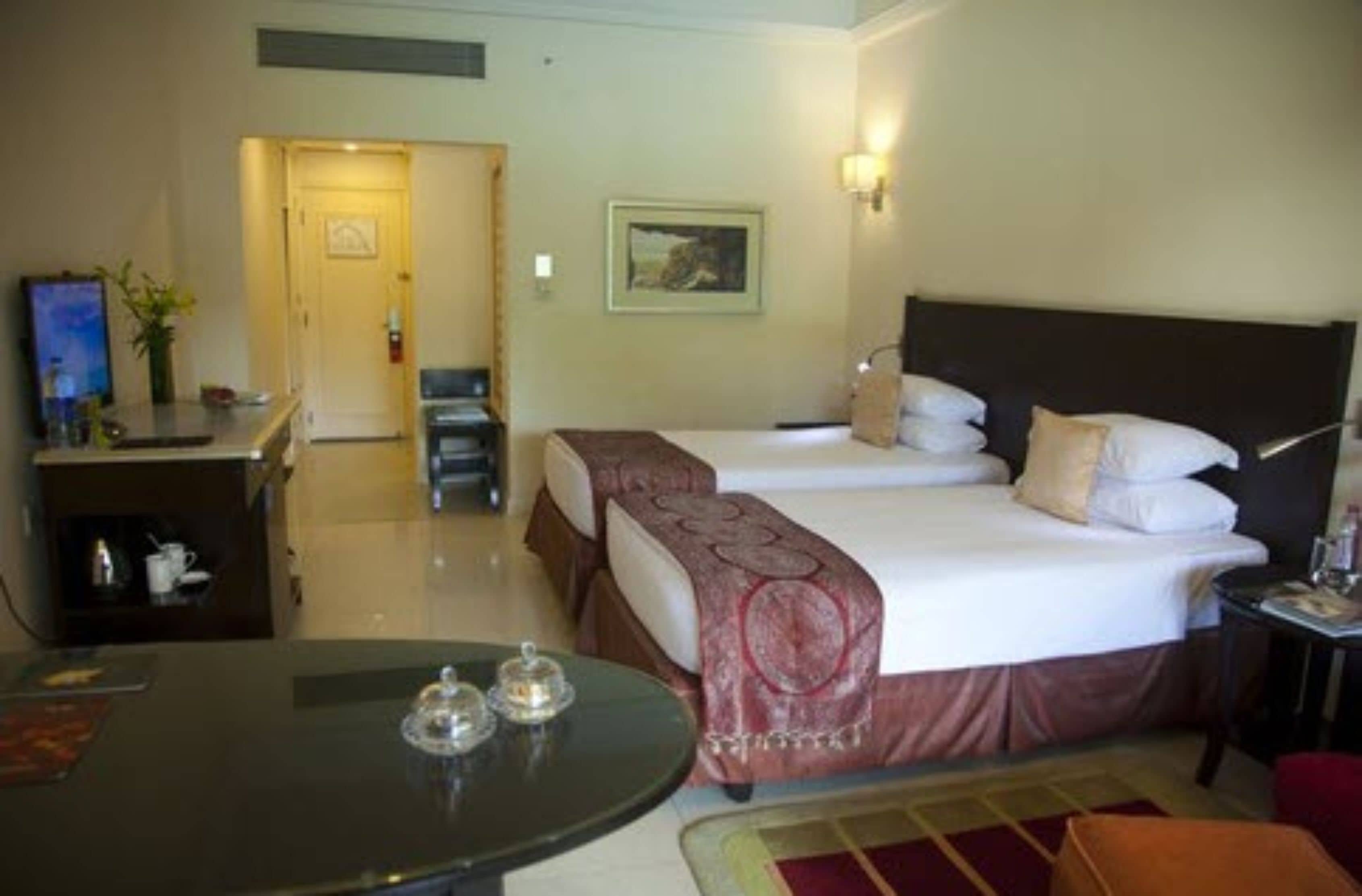 A hotel room with a bed, bedside table, and a small table with two cups.