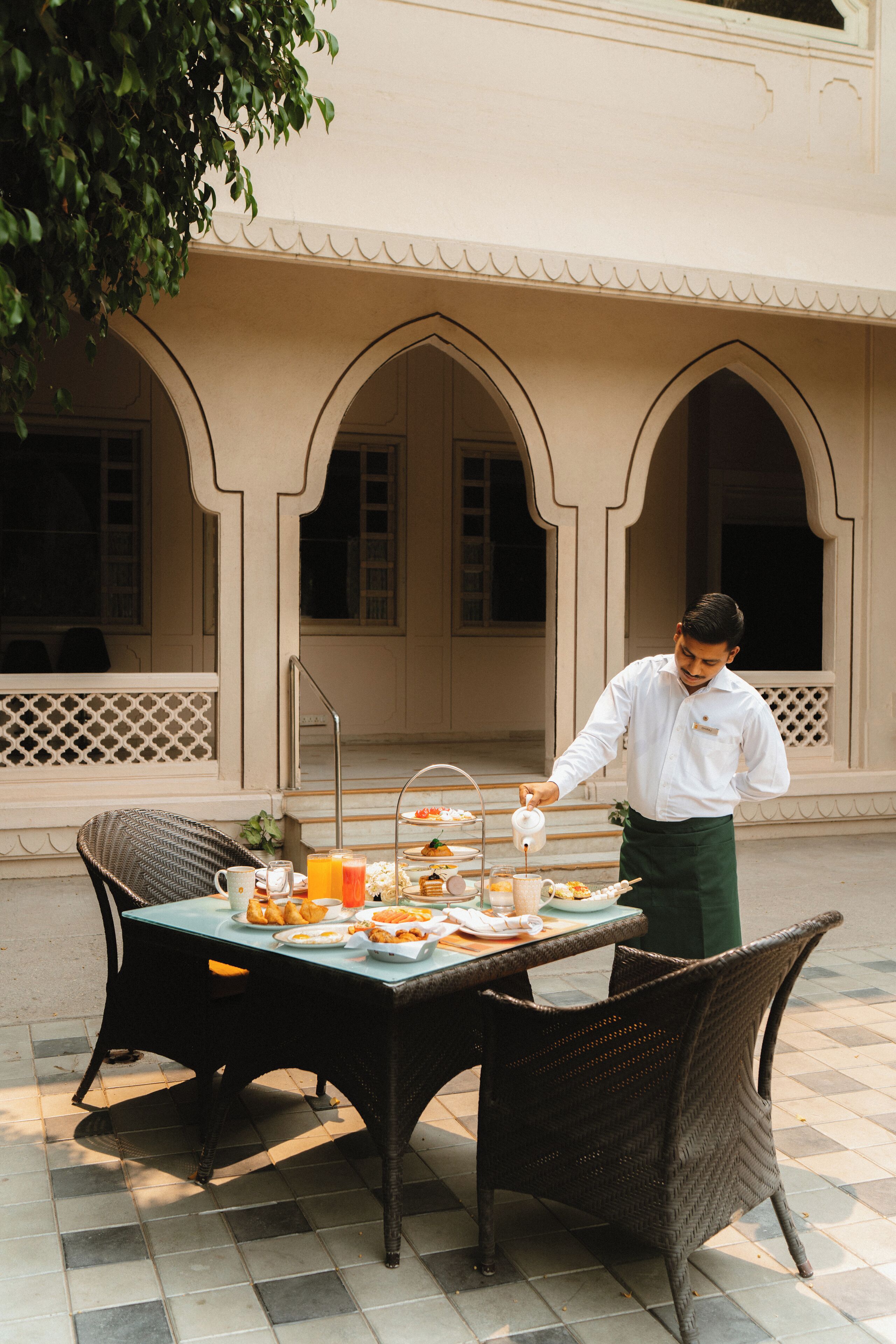 A waiter serving breakfast at an outdoor table with a view of a building with arches.