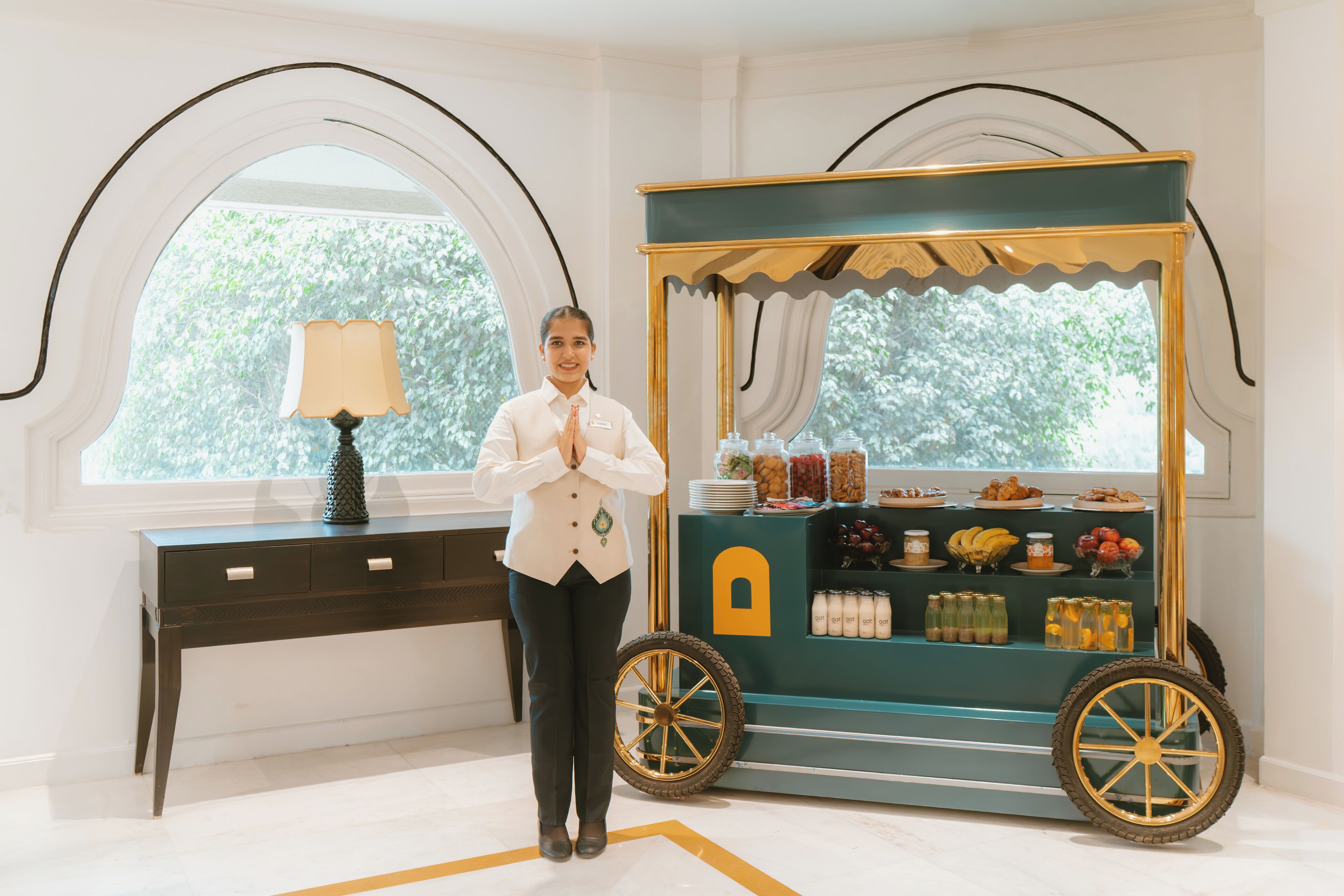 A person standing next to a food cart with various food items and a lamp on a desk.