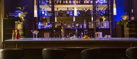 A bar area with multiple shelves of liquor bottles, a bar counter, and three black bar stools.