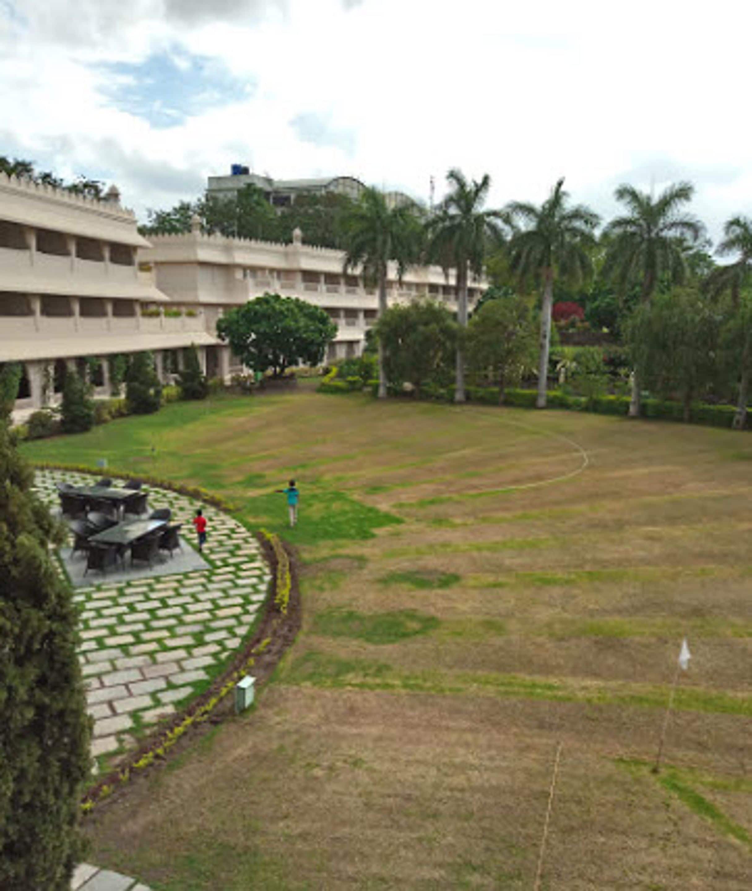 A courtyard with a lawn, a paved area with tables and chairs, and a building with multiple floors and balconies.