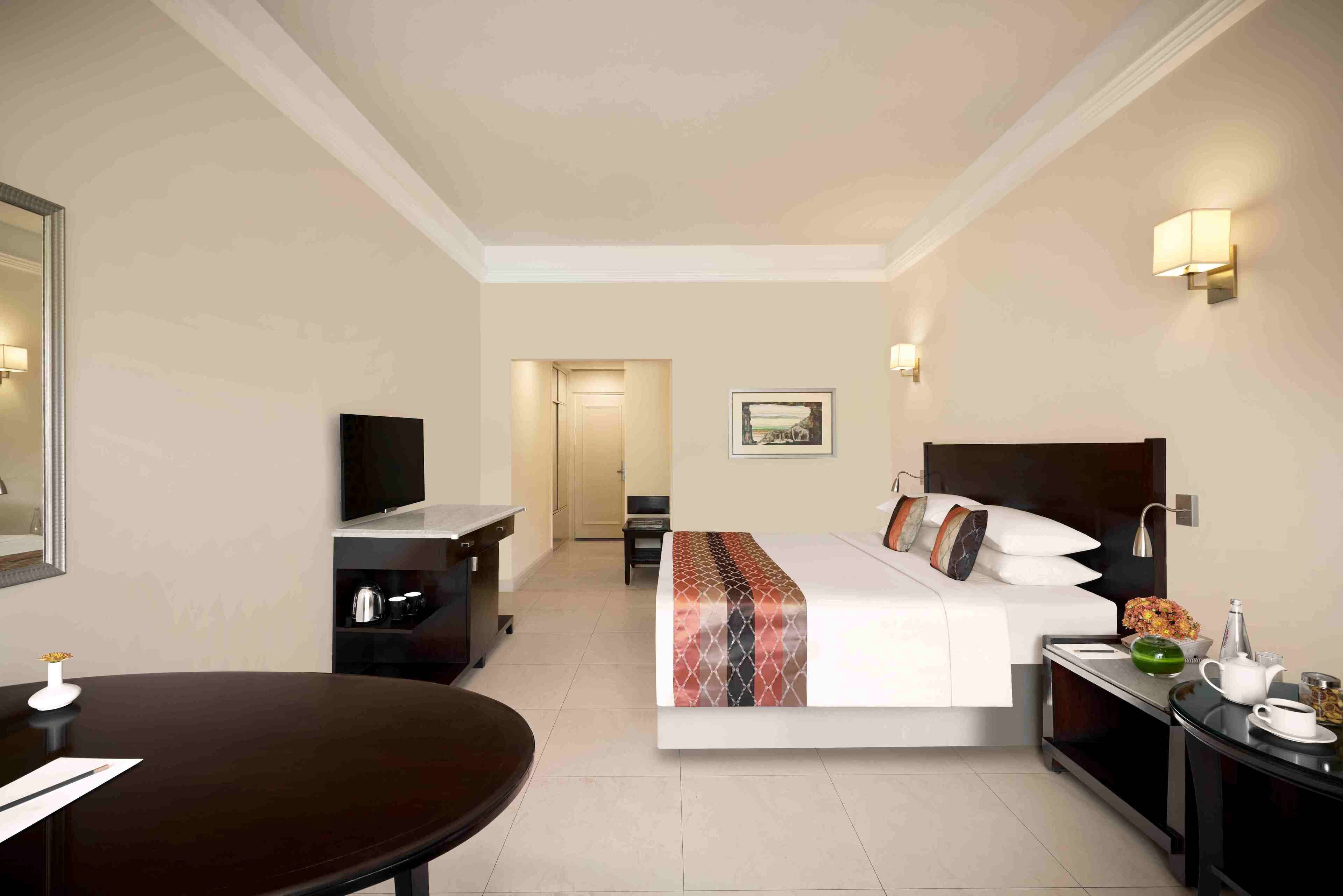 A hotel room with a bed, a desk, a chair, a TV, a bedside table with a lamp, and a picture on the wall.