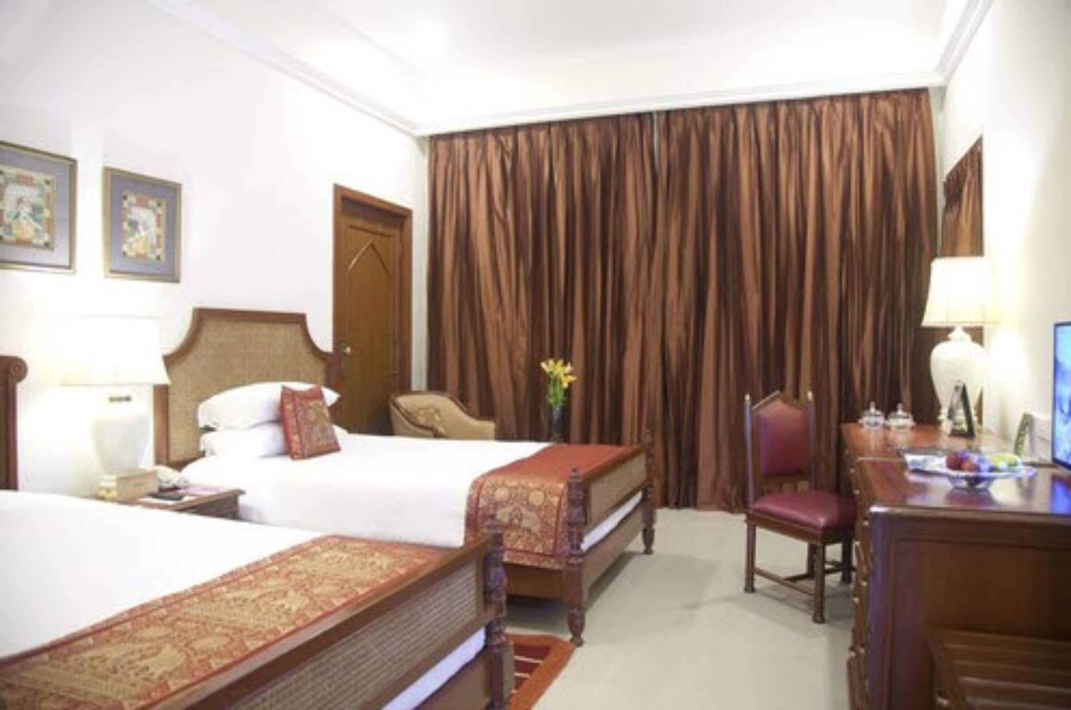 Une chambre d’hôtel avec deux lits, un bureau, une chaise et une grande fenêtre avec des rideaux.