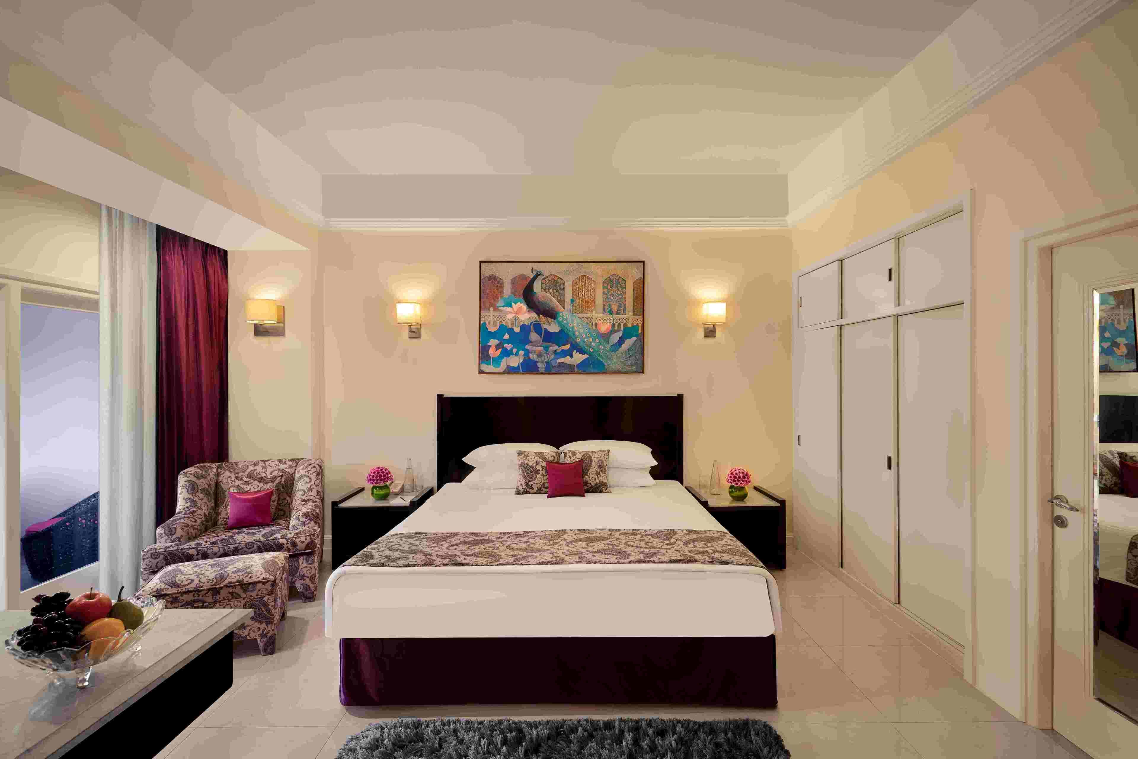A bedroom with a large bed, a chair, a nightstand, a painting, and a wardrobe.