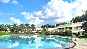 A swimming pool surrounded by a landscaped garden with palm trees and a building with traditional architecture in the background. - Gateway Aurangabad - Chhatrapati Sambhaji Nagar (Chhatrapati Sambhajinagar)
