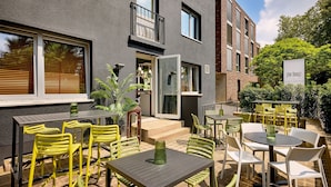 An outdoor patio area with tables and chairs, a door leading to a building, and a sign that reads "the Douz." - The Deutz, a Tribute Portfolio Hotel by Marriott (Cologne)