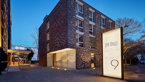 A modern building with a brick facade, large windows, and a prominent entrance. - The Deutz, a Tribute Portfolio Hotel by Marriott (Cologne)