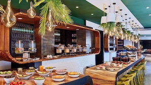 A buffet setup with various food items and a bar area with bottles and glasses. - The Deutz, a Tribute Portfolio Hotel by Marriott (Cologne)