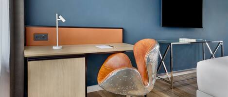 Une chambre d’hôtel moderne équipée d’un bureau en bois, d’un fauteuil pivotant, d’un téléviseur à écran plat et d’une petite table avec une télécommande.