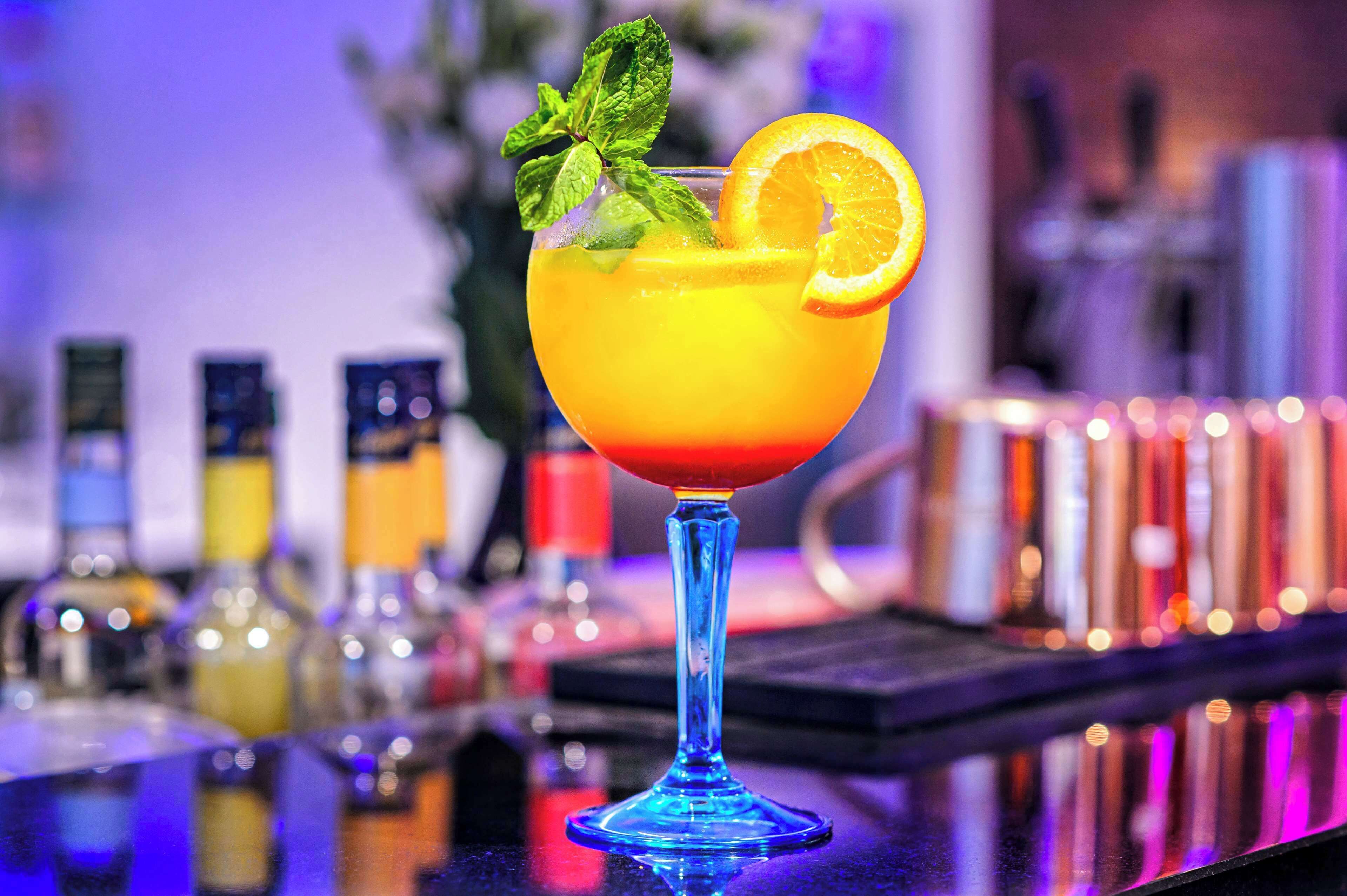Een cocktail in een blauw glas, met een oranje schijfje en munt.