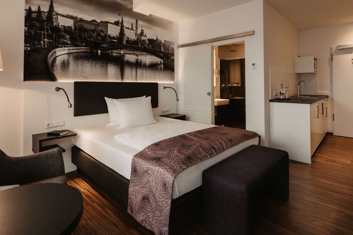 Une chambre d’hôtel moderne, dotée d’un grand lit, d’un bureau et offrant une vue sur le paysage urbain.