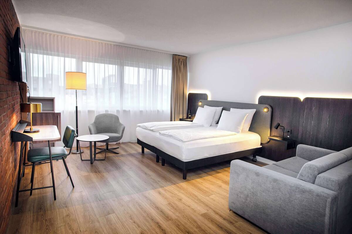 A hotel room with a bed, a desk, a chair, and a sofa.