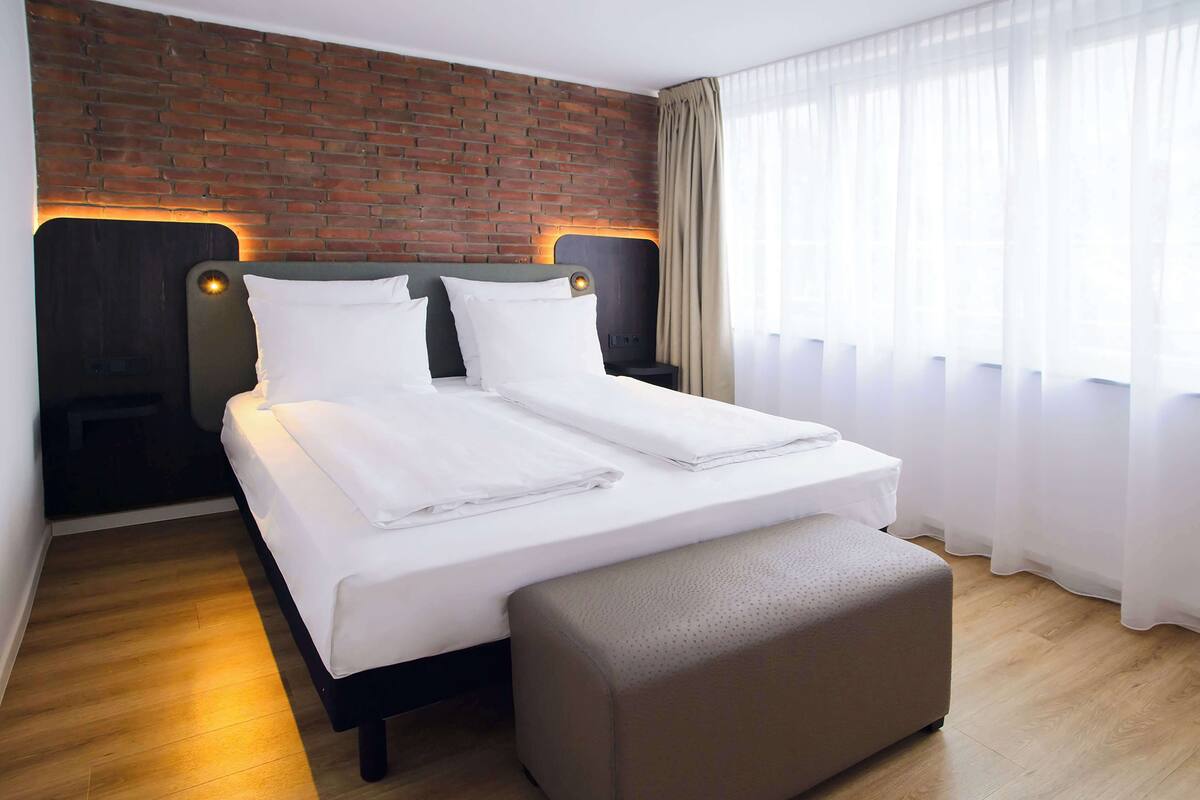 A neatly made bed with white linens, a wooden headboard, and a small bedside table with a lamp.