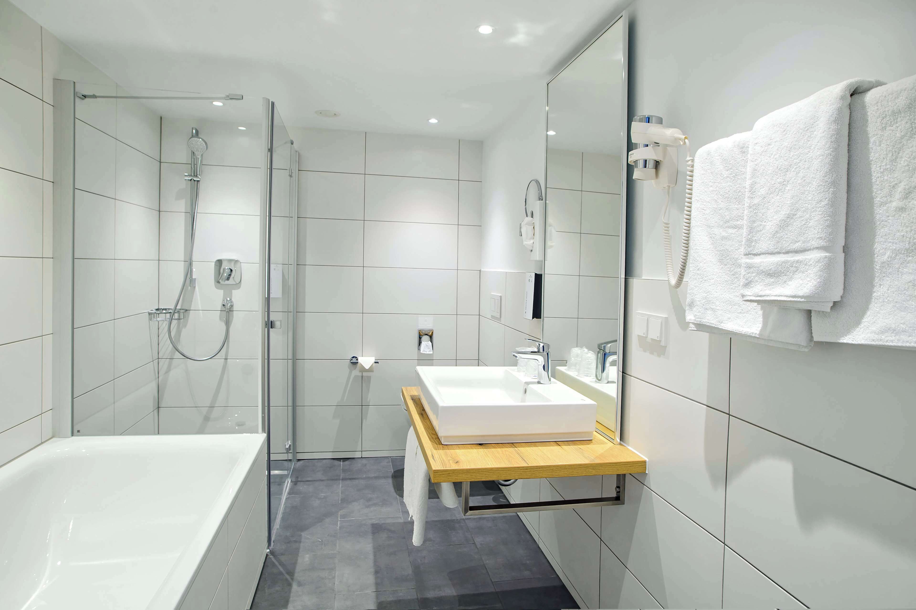 Ein modernes Badezimmer mit einer gläsernen Duschkabine, einer freistehenden Badewanne und einem hölzernen Waschtisch mit weißem Waschbecken.
