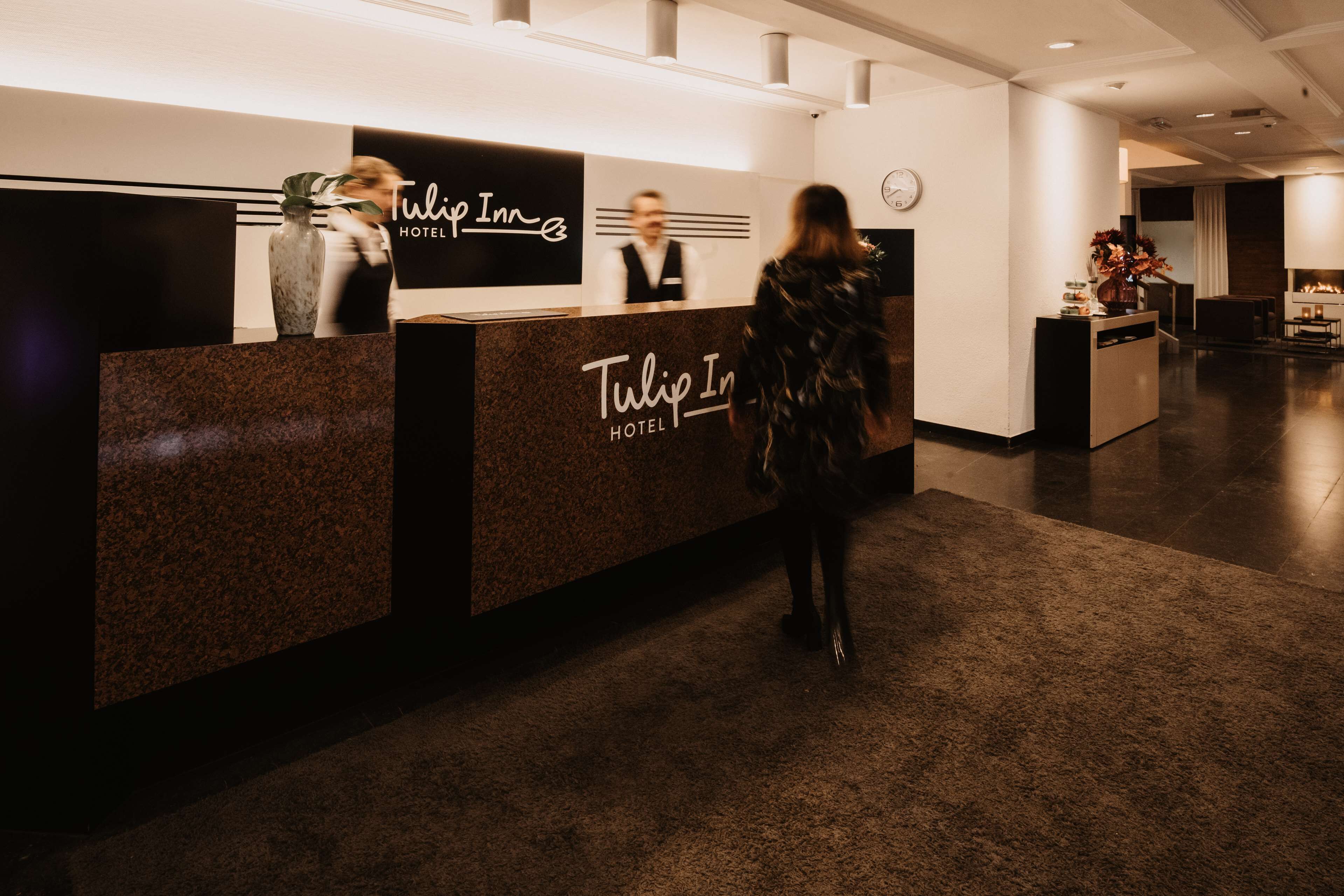 Un mostrador de recepción de hotel con diseño moderno, un reloj y una zona de estar al fondo.