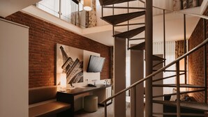 A modern interior with a brick wall, a staircase, a flat-screen TV, and a bench.