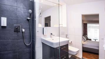 Un baño moderno con ducha, inodoro y lavabo, y un dormitorio con cama y ventana.