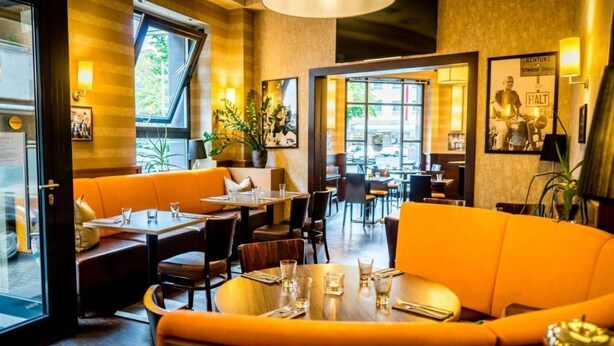 Un restaurante con una decoración moderna, que ofrece una variedad de opciones de asiento, como mesas y sofás, y vistas a la calle a través de amplios ventanales.