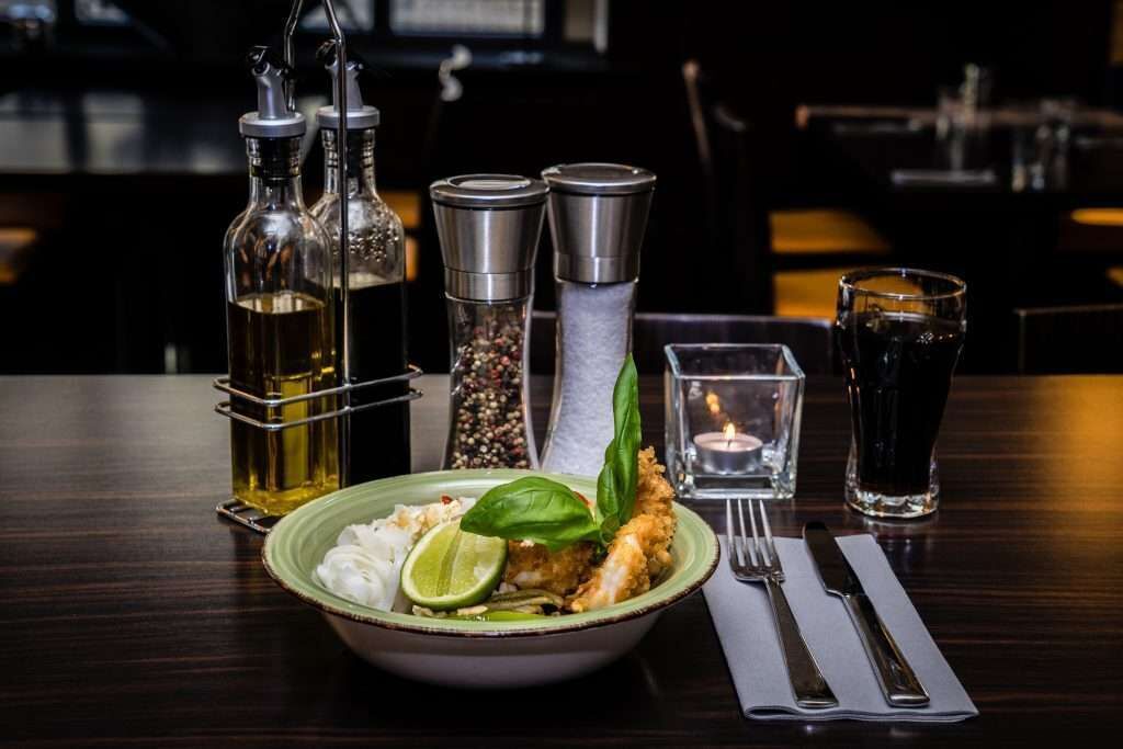 A dining table with a bowl of food, a bottle of oil, salt and pepper shakers, a glass of water, and a candle.