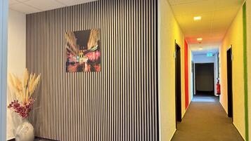 A hallway with a striped wall, a framed picture, and a vase with dried plants.