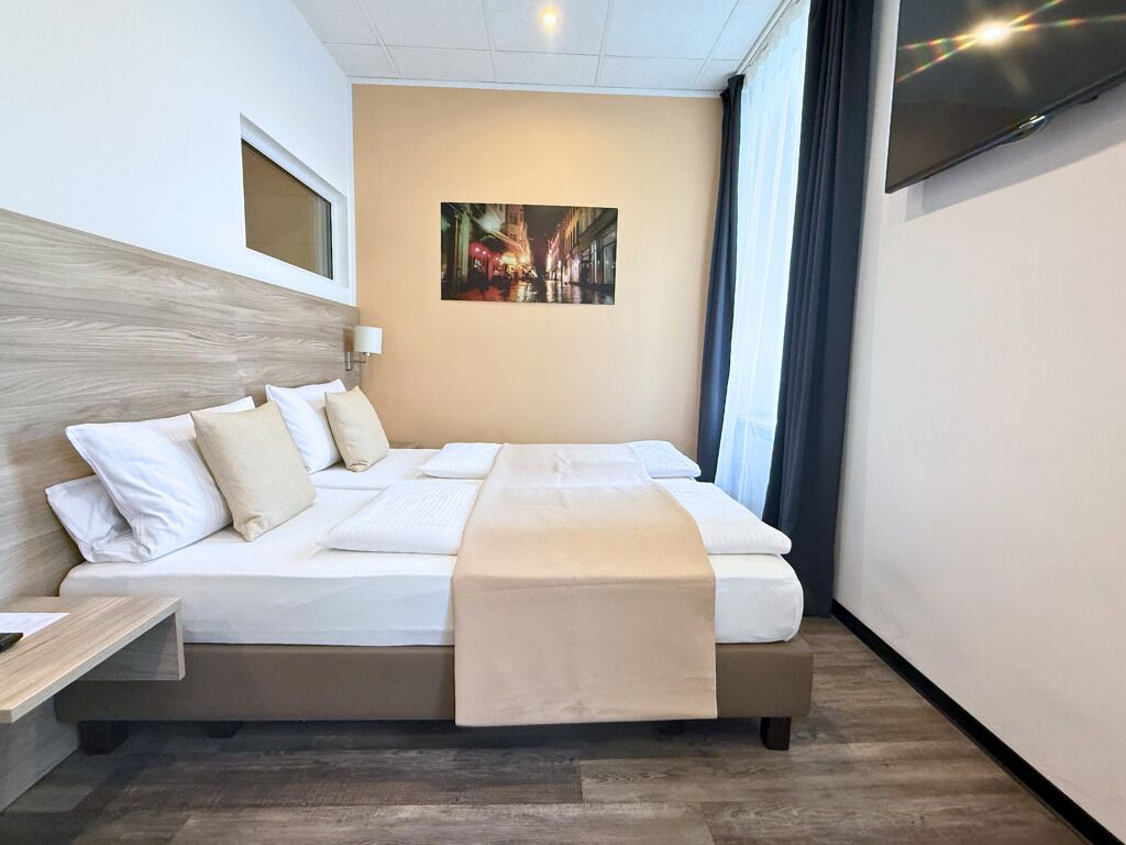 A hotel room with a bed, a nightstand, a painting on the wall, and a TV on the wall.