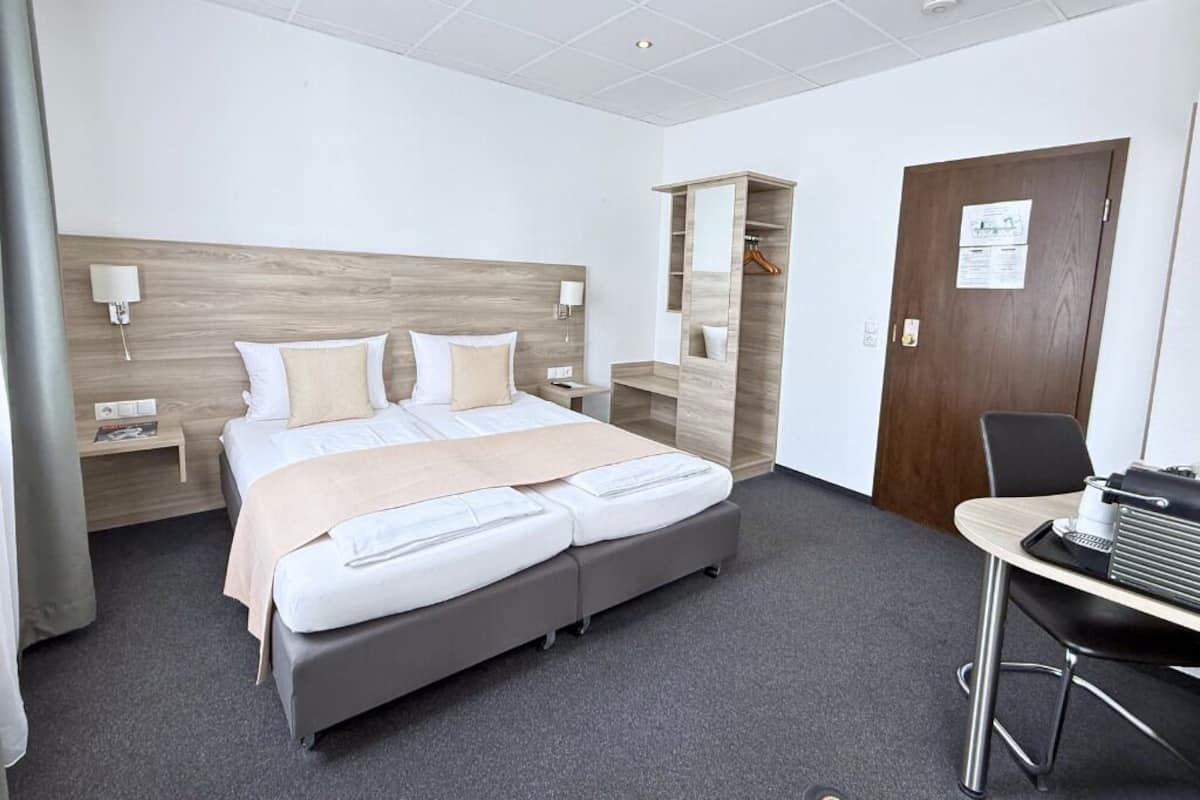 A hotel room with a bed, bedside tables, a desk, and a chair.