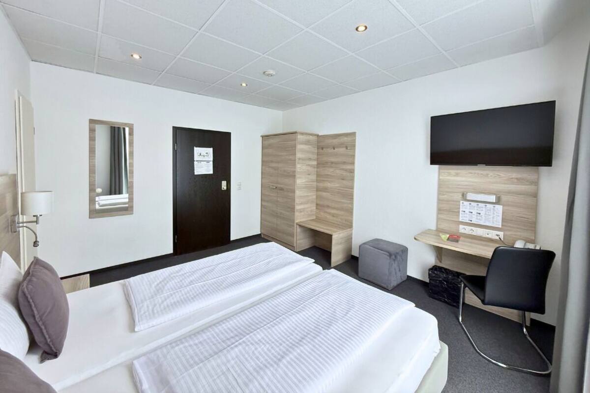 A hotel room with a bed, a desk, a chair, a TV, and a wardrobe.