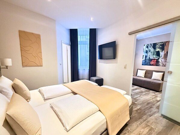 Una habitación de hotel con cama, sofá, televisor y un cuadro en la pared.