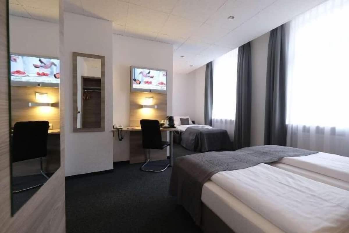 A hotel room with a bed, a desk with a chair, a television, and a window with curtains.