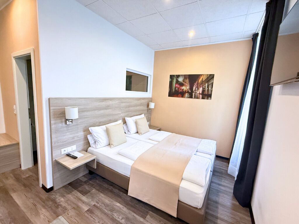 Ein Hotelzimmer mit einem großen Bett, Nachttischen, einem Fenster und einem an der Wand hängenden Bild.