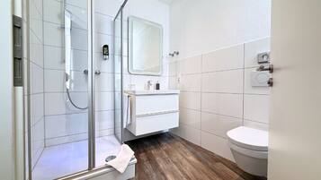 A modern bathroom with a glass shower enclosure, a white sink, and a toilet.