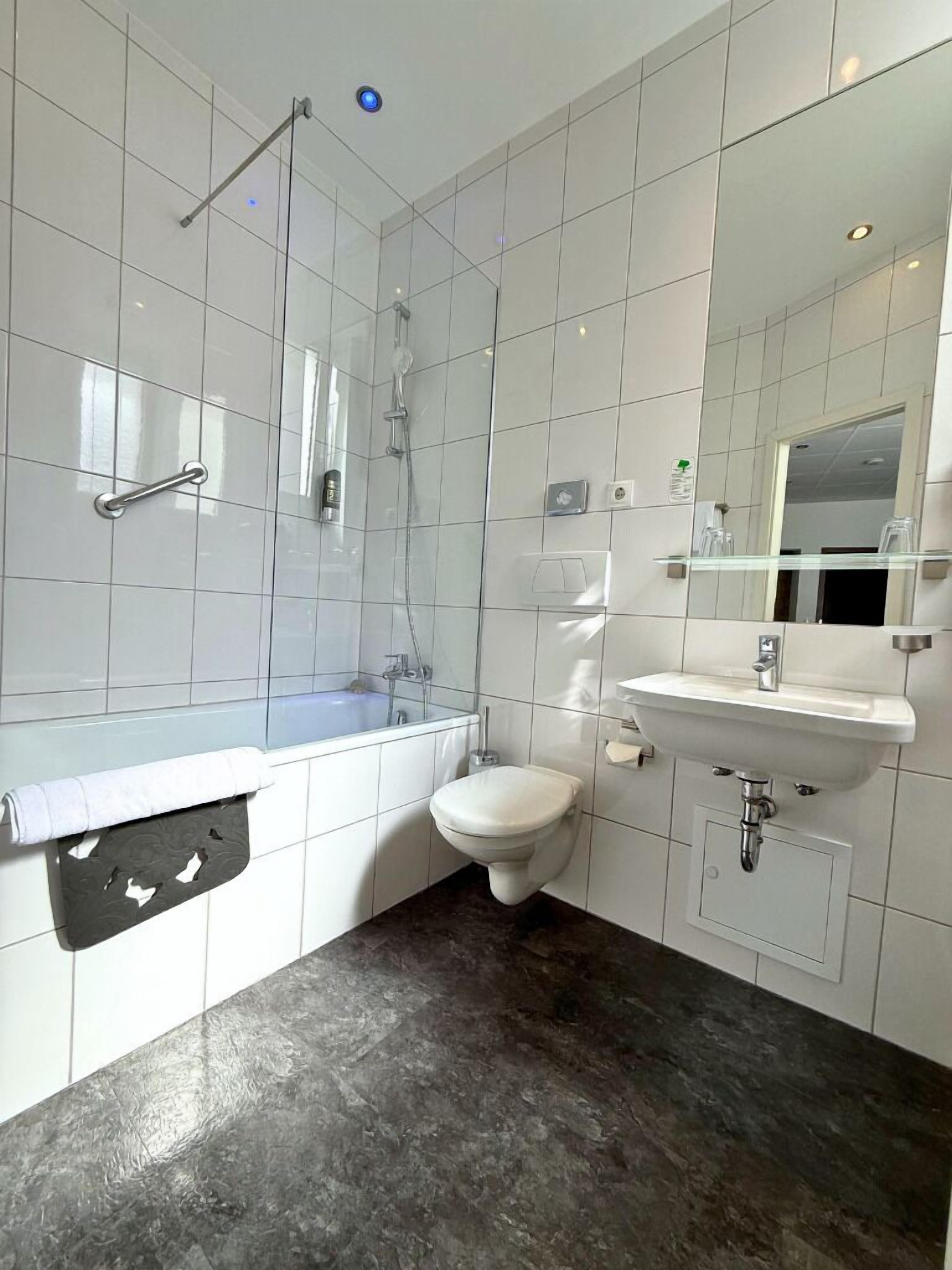 A bathroom with white tiles, a bathtub, a toilet, a sink, and a mirror.