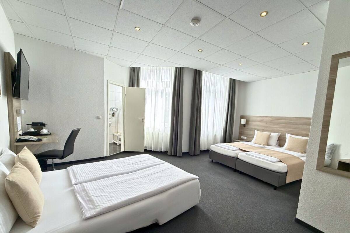 A hotel room with a large bed, a smaller bed, a desk with a chair, a TV, and a bathroom door.