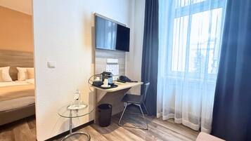 A hotel room with a bed, a desk with a chair, a TV, and a window with curtains.