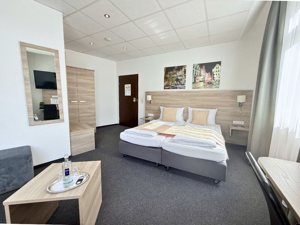 A hotel room with a bed, a bedside table with a tray, a mirror, a wardrobe, and a wall-mounted TV.