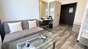 Una habitación de hotel moderna con sofá, una mesita de vidrio, escritorio con silla y armario.