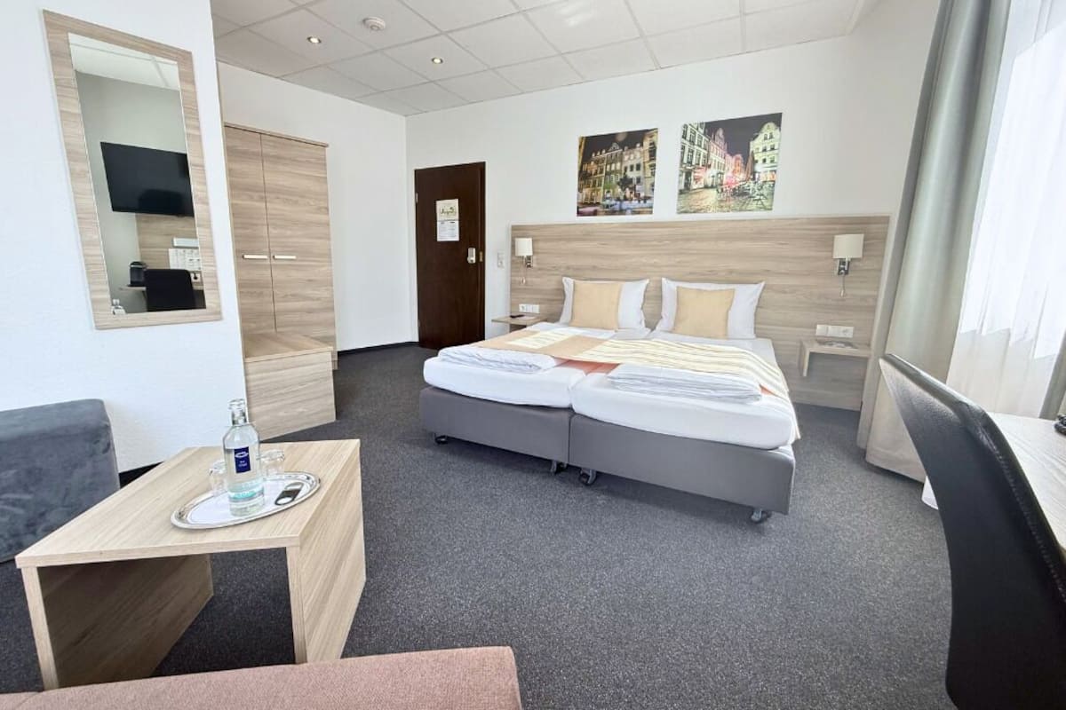A hotel room with a bed, bedside tables, a desk, a chair, a mirror, and artwork on the wall.