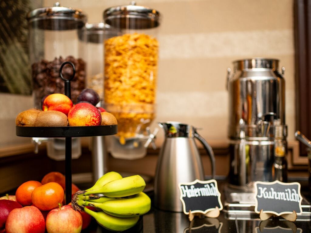 A buffet setup with fruits, a coffee pot, and two labeled signs.