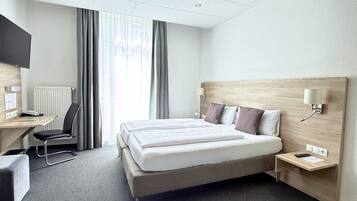 A hotel room with a bed, bedside table, lamp, desk, chair, and a television.