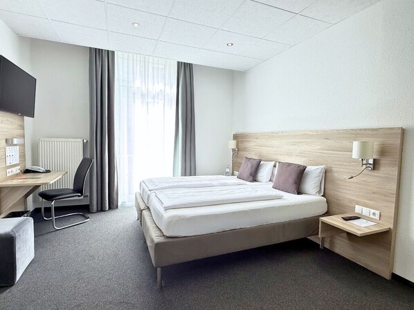 Una habitación de hotel con cama, mesita de noche, lámpara, escritorio, silla y televisor.